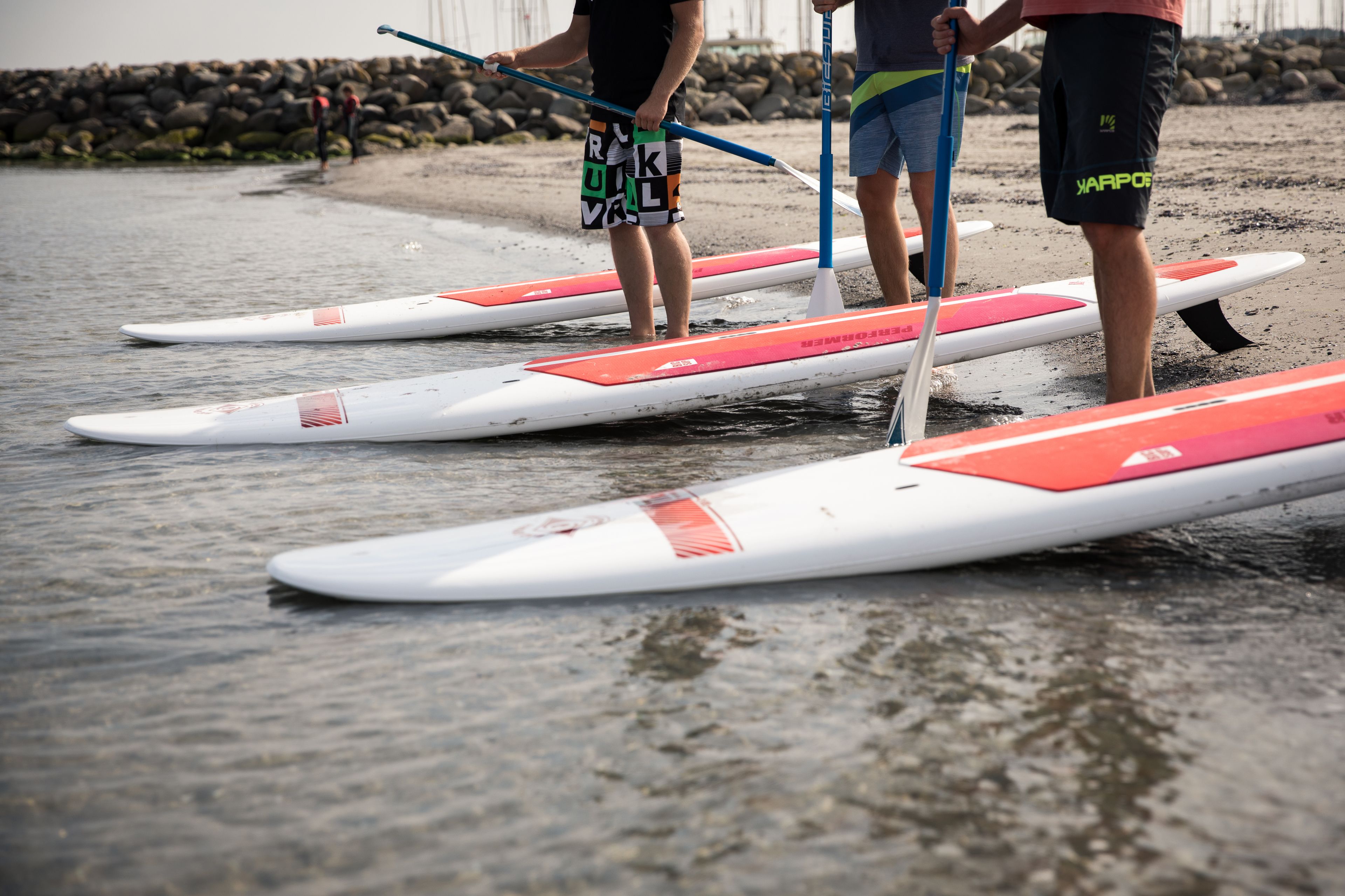 Three paddleboards on a sandy beach with a rocky shoreline in the background.