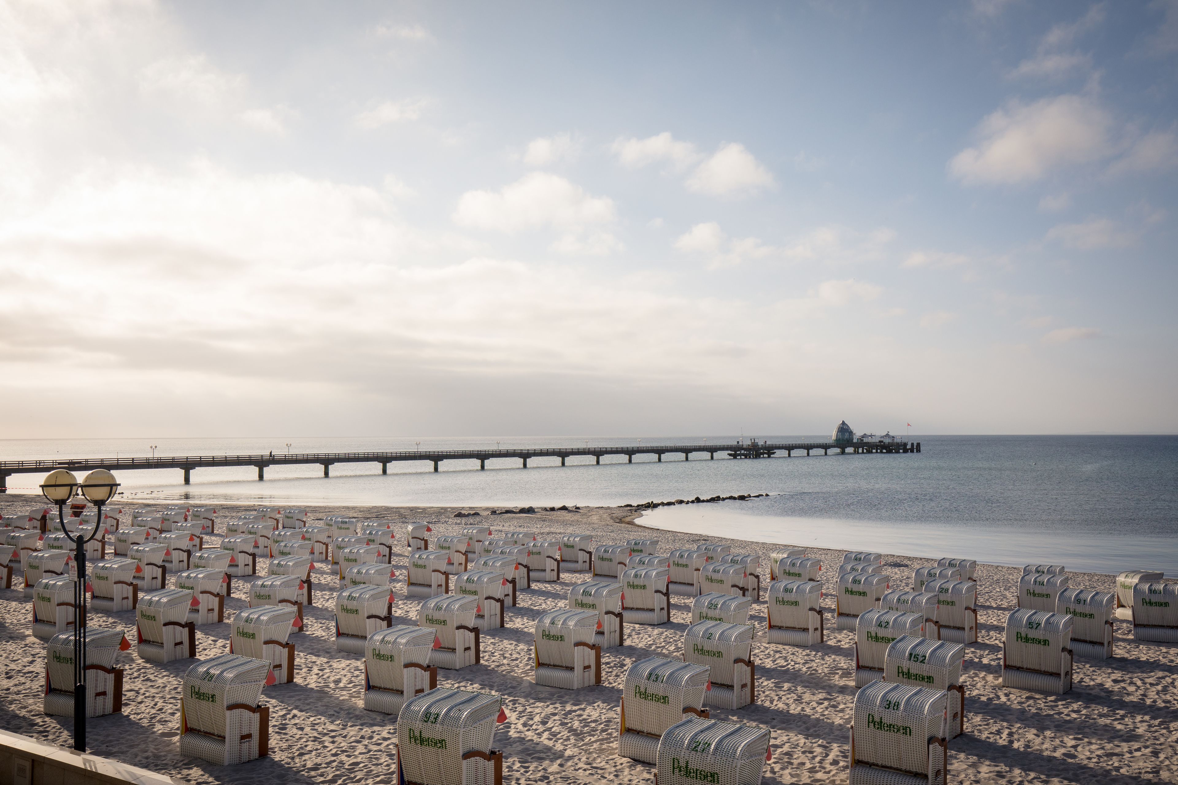 A beach with rows of beach chairs labeled "Pelikan" and a pier extending into the water.
