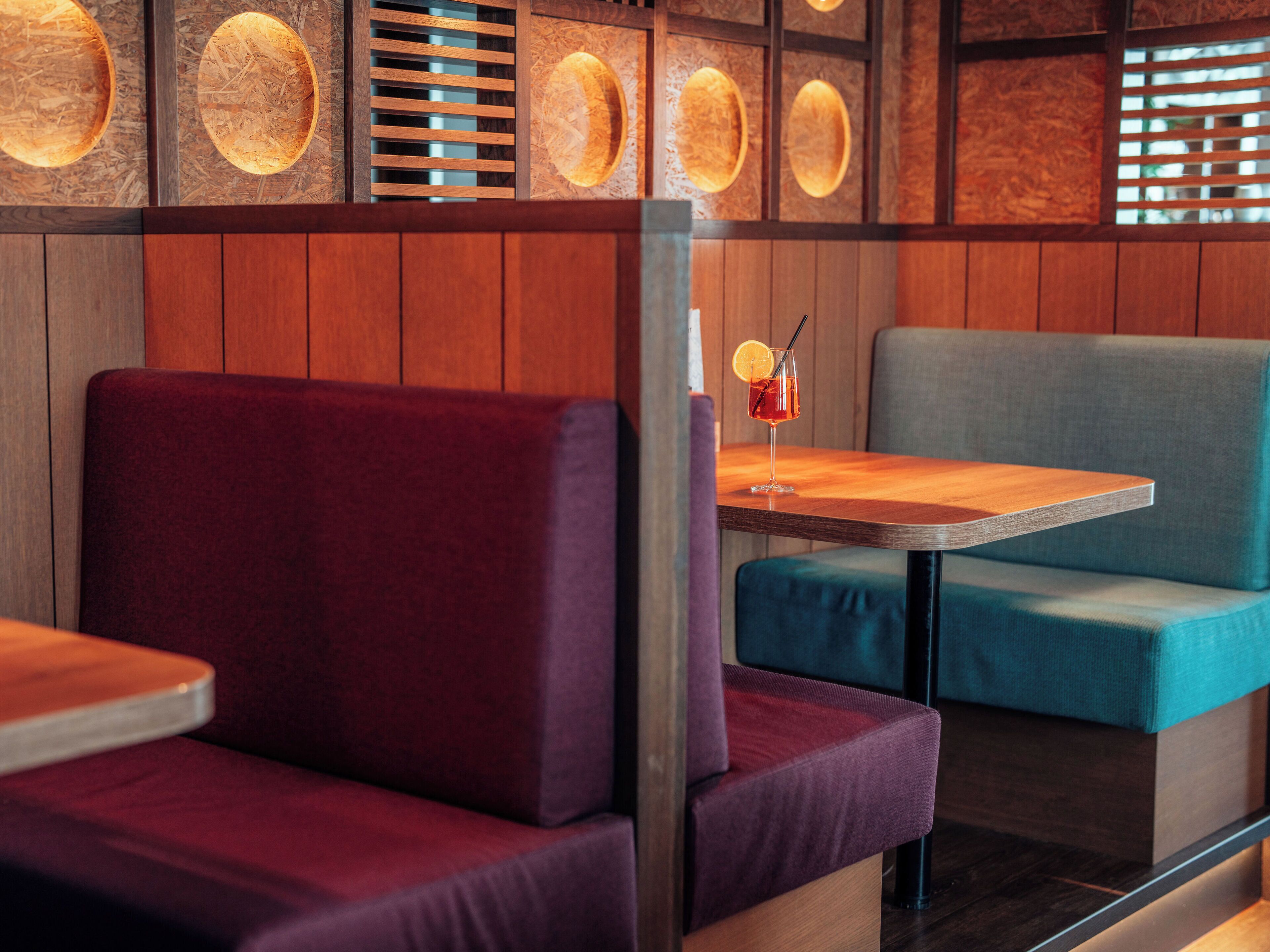 Een restaurantinterieur met houten lambrisering, gestoffeerde zitmogelijkheden en een tafel met een drankje.