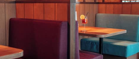 A restaurant interior with wooden paneling, cushioned seating, and a table with a drink.