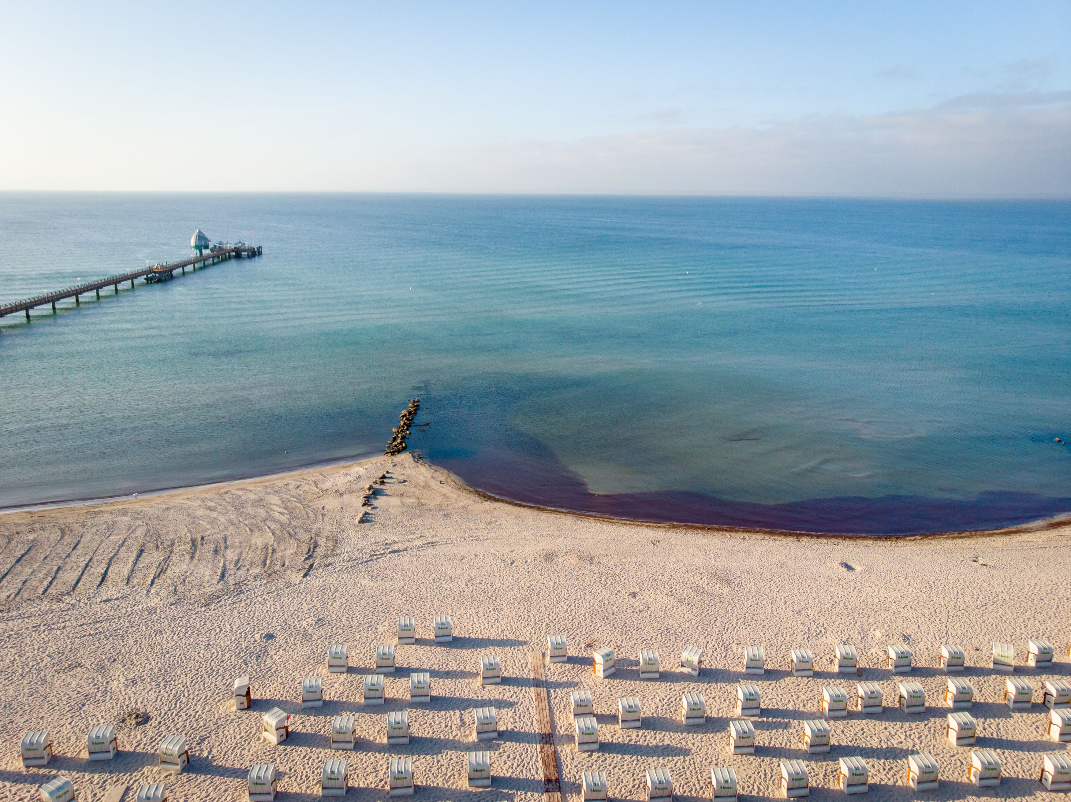 A beach with rows of beach huts and a pier extending into the sea.