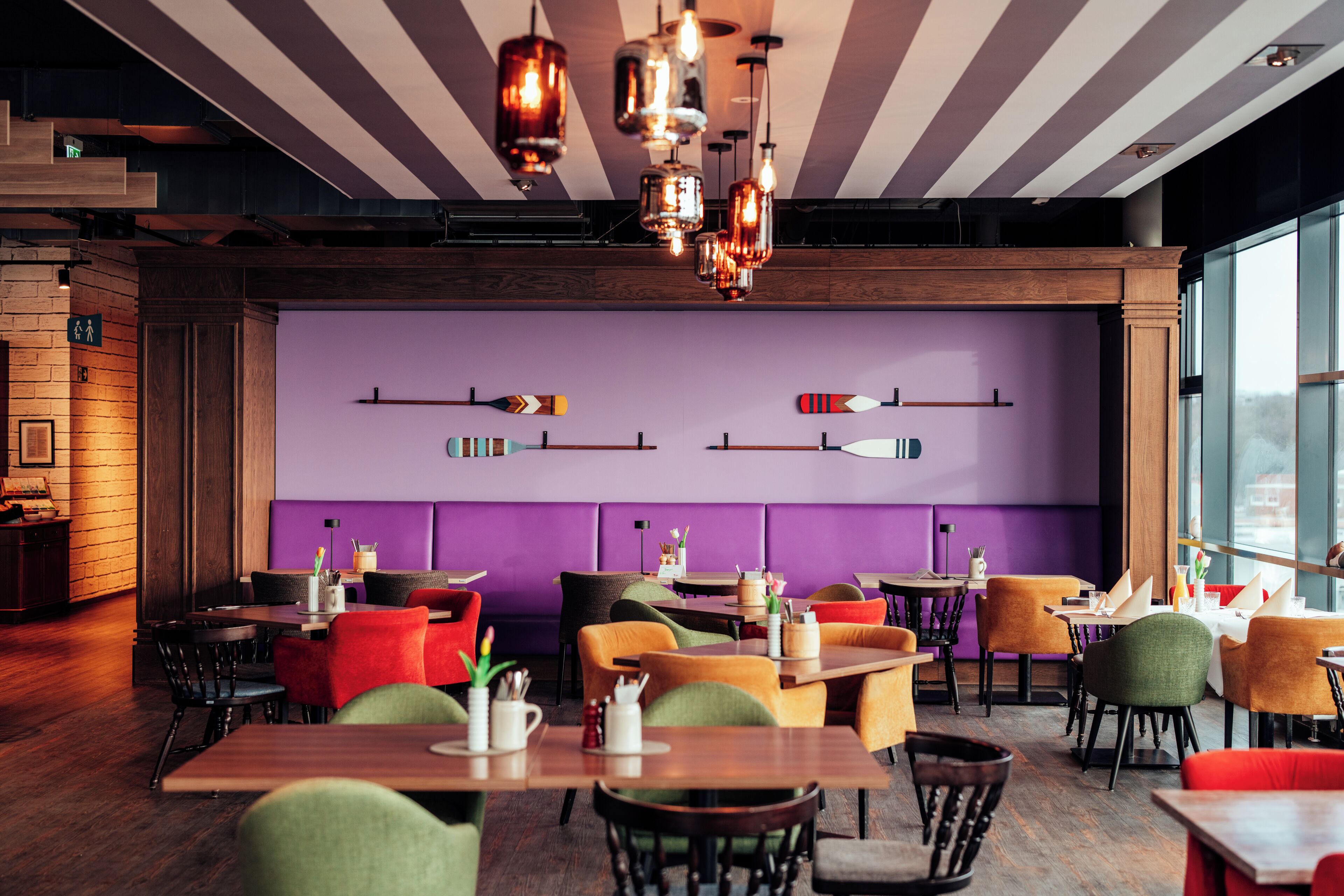 A restaurant interior with wooden tables, colorful chairs, and pendant lighting.