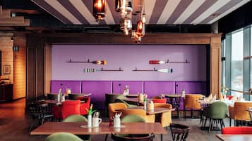 Un interior de restaurante con mesas de madera, sillas de colores e iluminación colgante.