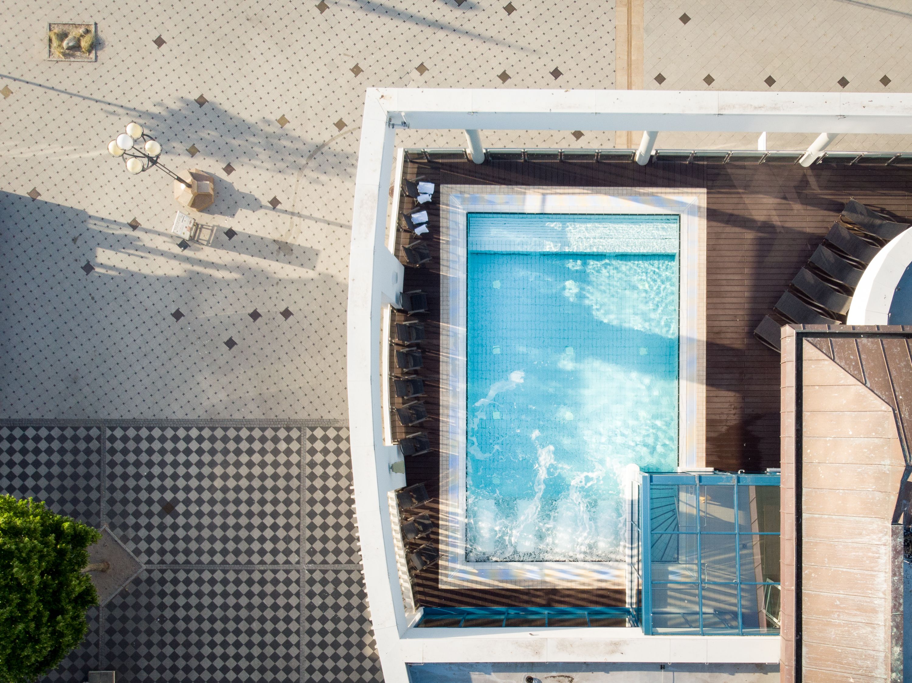 A rooftop pool with a tiled deck, a seating area, and a view of the surrounding area.