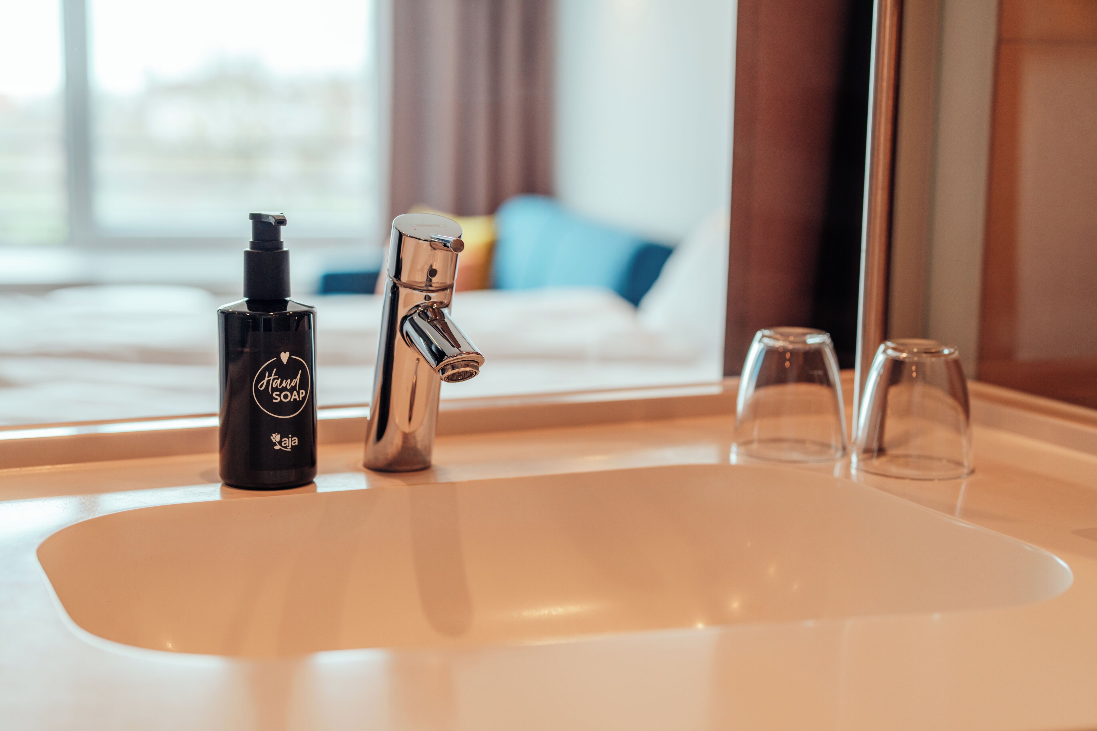 Un lavabo de salle de bain avec un distributeur de savon liquide, un robinet et deux verres.