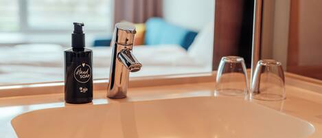 A bathroom sink with a hand soap dispenser, a faucet, and two glasses.
