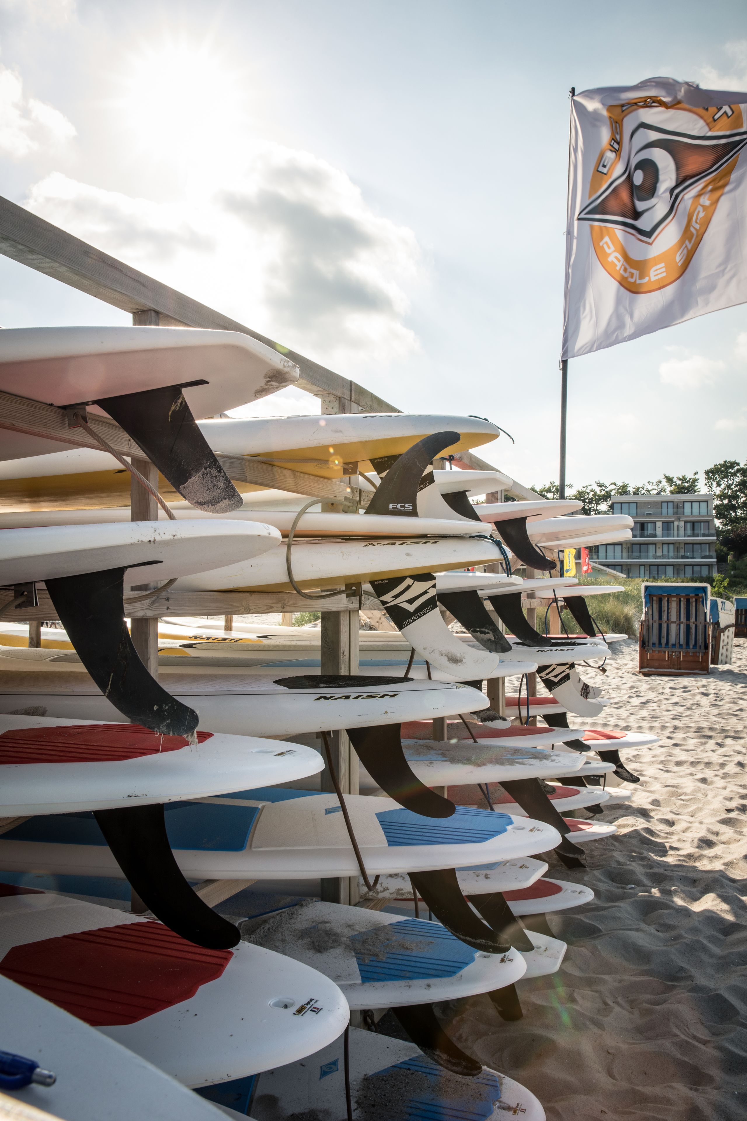 Une rangée de planches de surf sur une plage, avec un drapeau en arrière-plan.