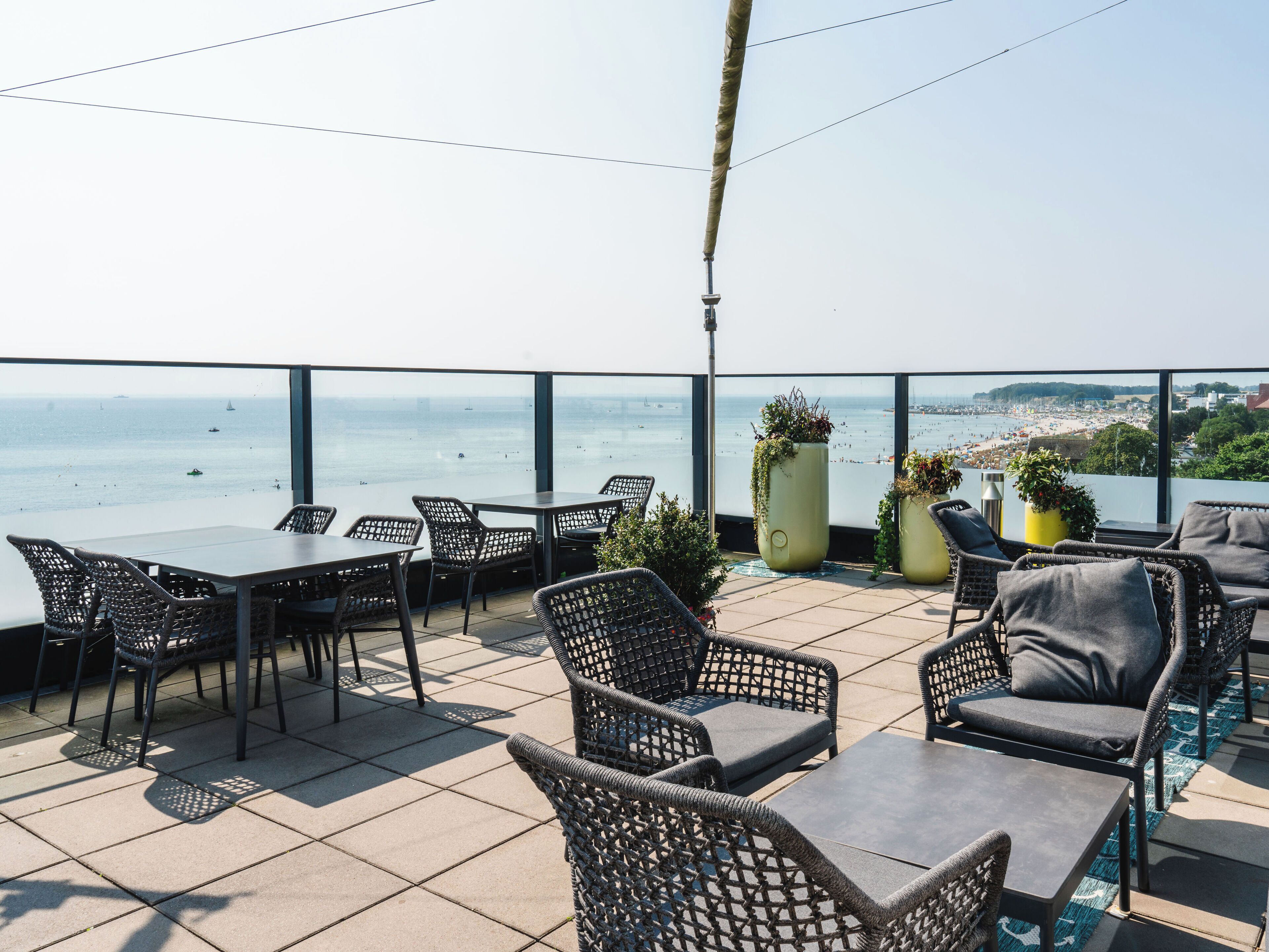 A terrace with wicker furniture, a view of the sea, and a cityscape in the background.