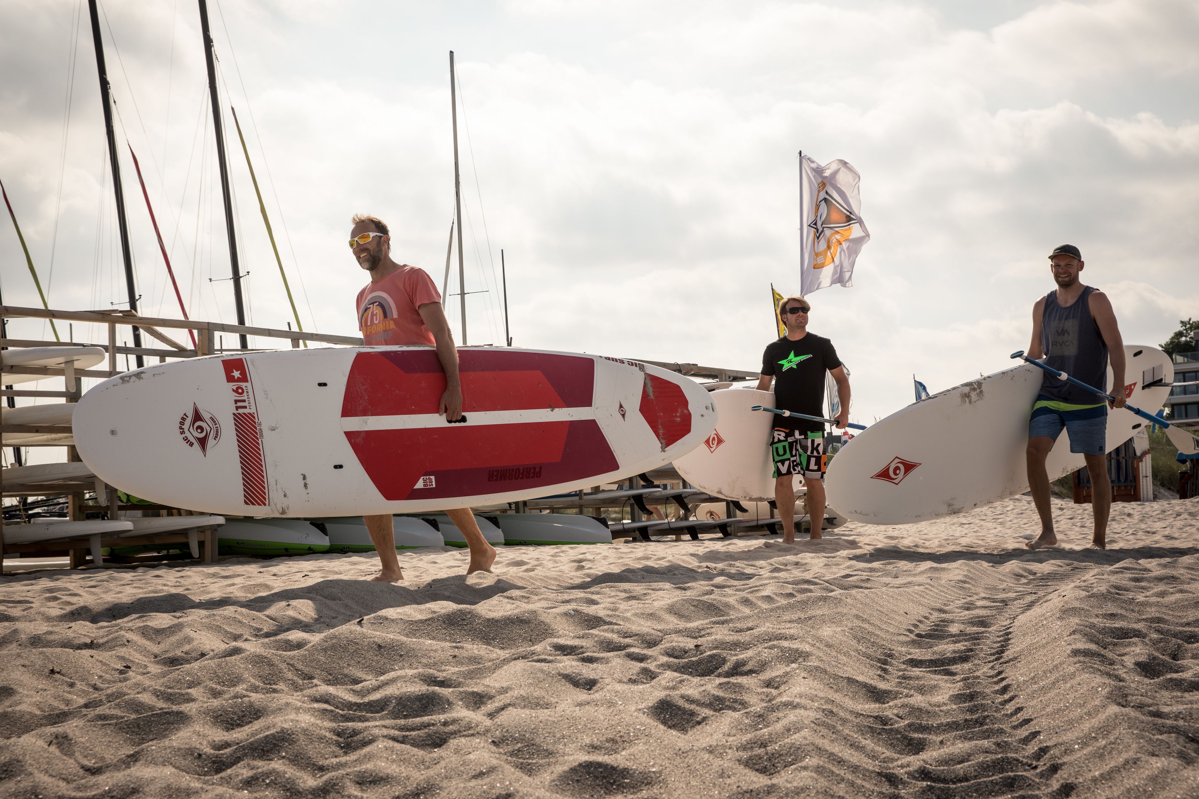 A sandy beach with three people carrying surfboards.