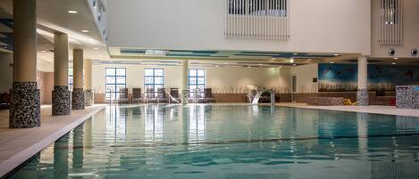 En indendørs swimmingpool med klart vand, fliserede vægge og et loft med indbygget belysning.