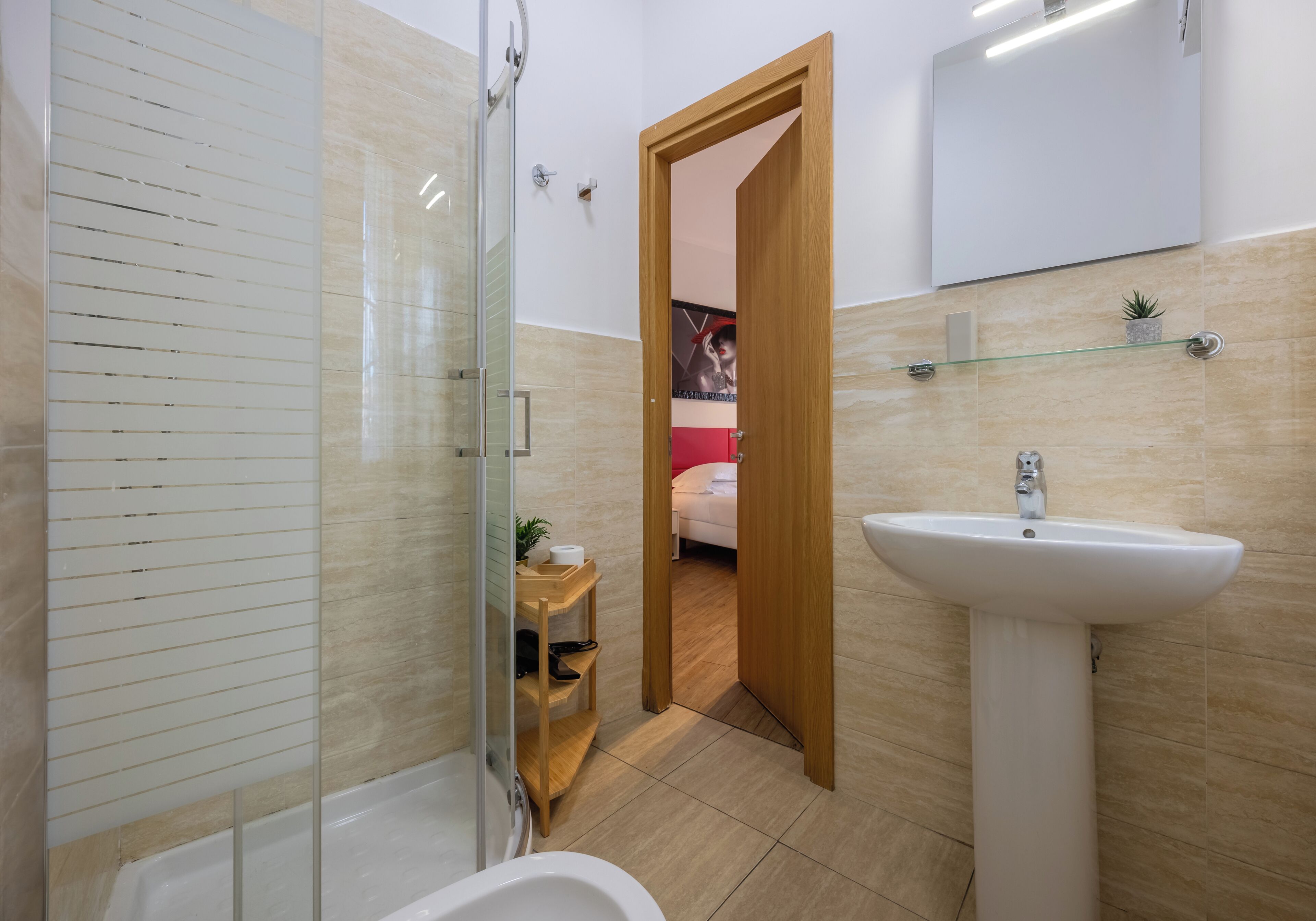 A modern bathroom with a glass shower enclosure, a white sink, and a wooden shelf with toiletries.