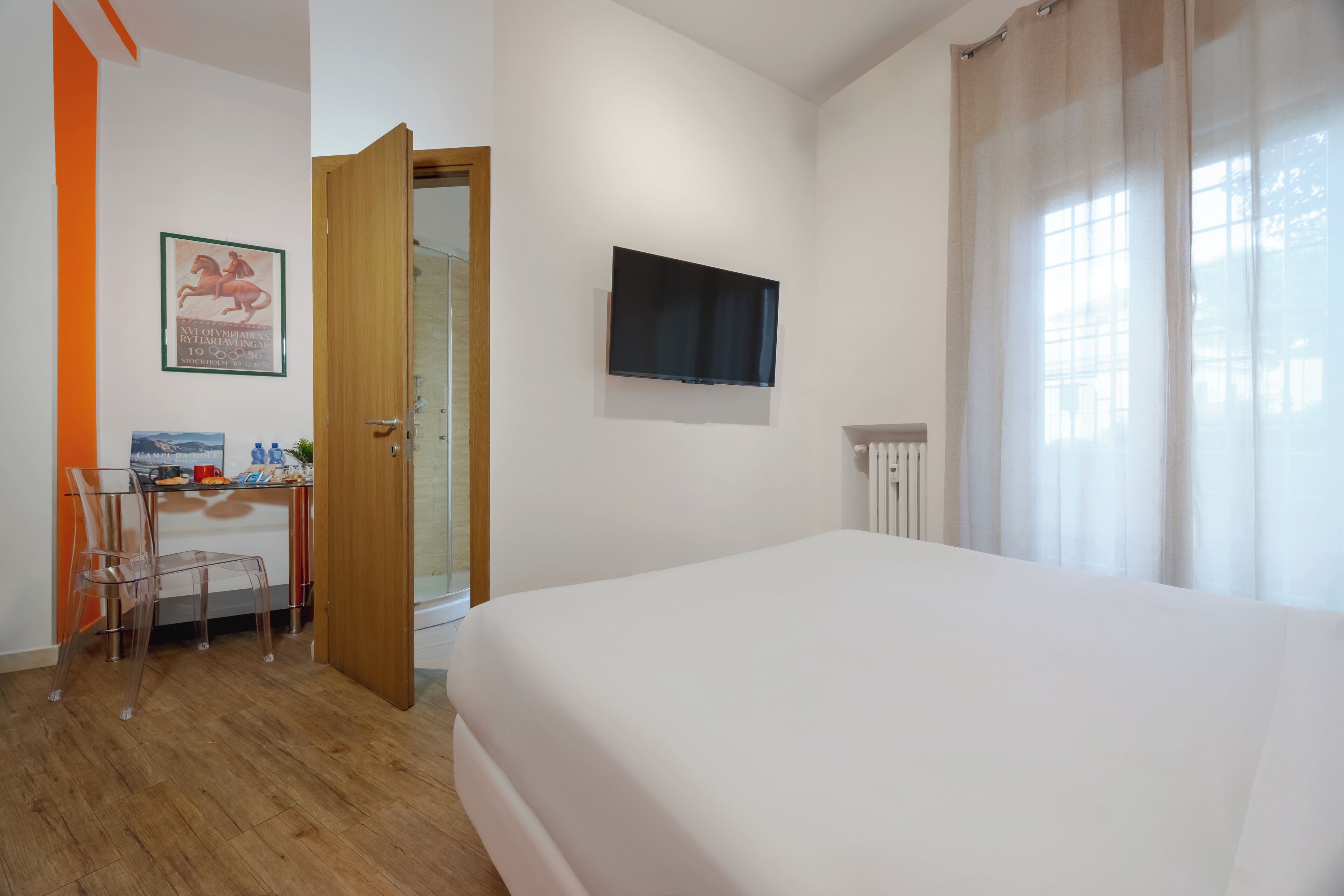 A hotel room with a bed, a desk with a chair, a TV, and a window with curtains.