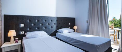 A hotel room with two beds, a nightstand, a lamp, and a view of the outdoors.