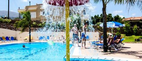 A swimming pool with a water fountain, lounge chairs, and a palm tree.