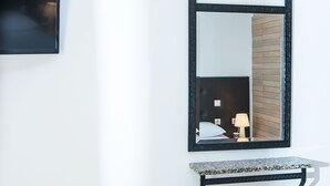A bathroom with a black-framed mirror, a small table with towels, and a wall-mounted light fixture. - Real Palace (Hersonissos)