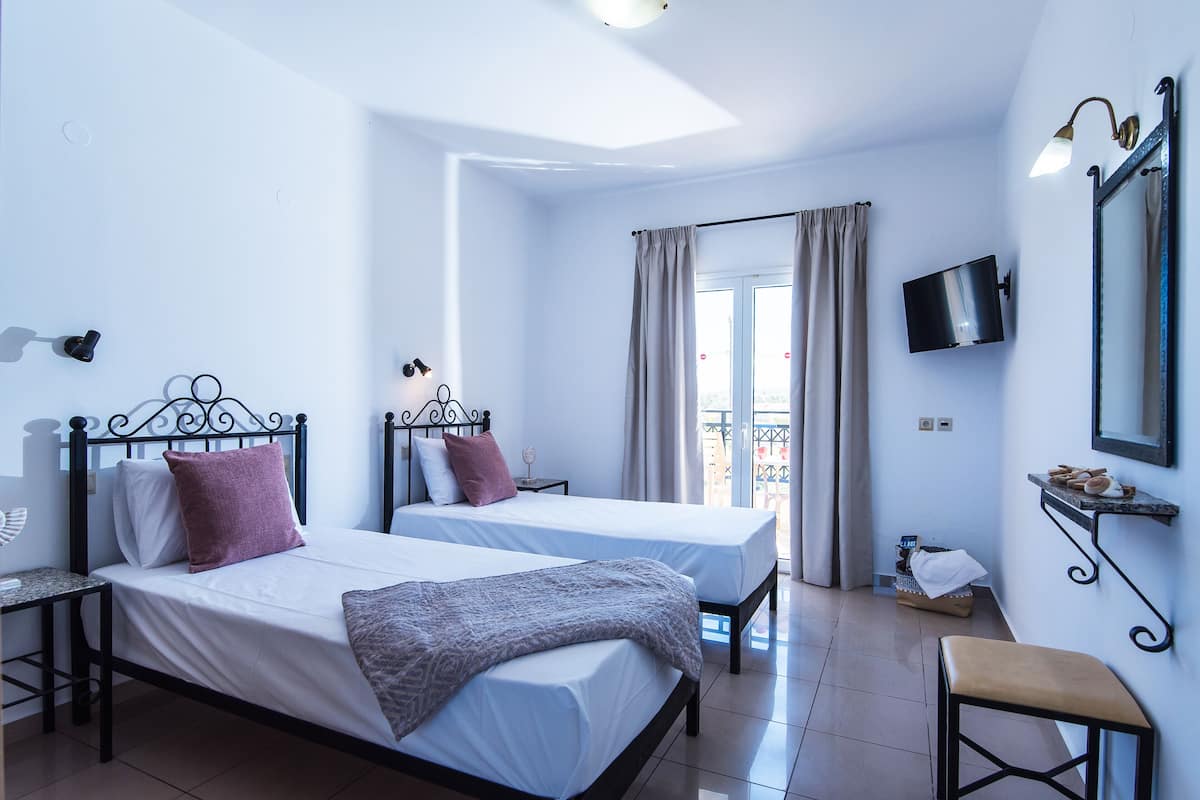 A hotel room with two beds, a TV, a balcony with curtains, and a small table.