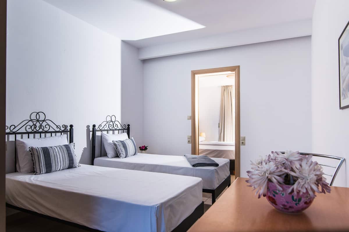 A hotel room with two single beds, a wooden table, a mirror, and a vase with flowers.