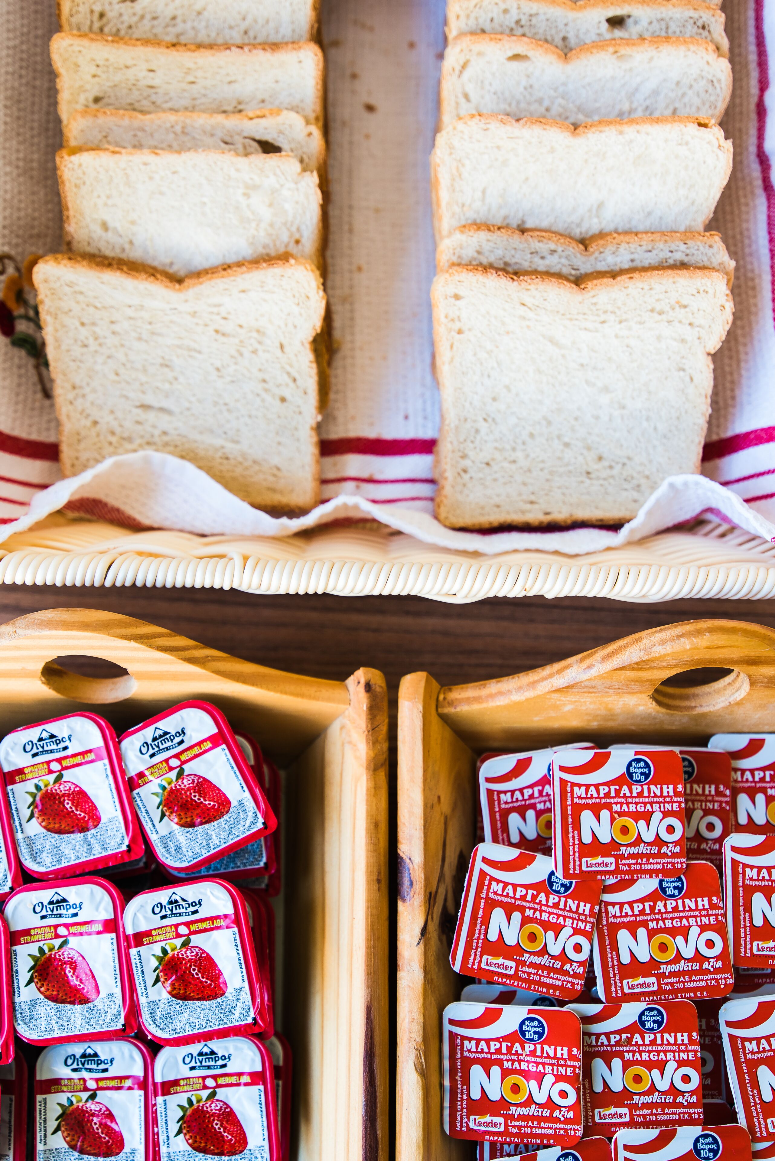 Des tranches de pain blanc et deux boîtes en bois contenant du yaourt au goût de fraise et de la margarine.