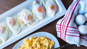 Un plato blanco con huevos pochados y revueltos, una cuchara y un paño de cocina con huevos desenfocados al fondo.