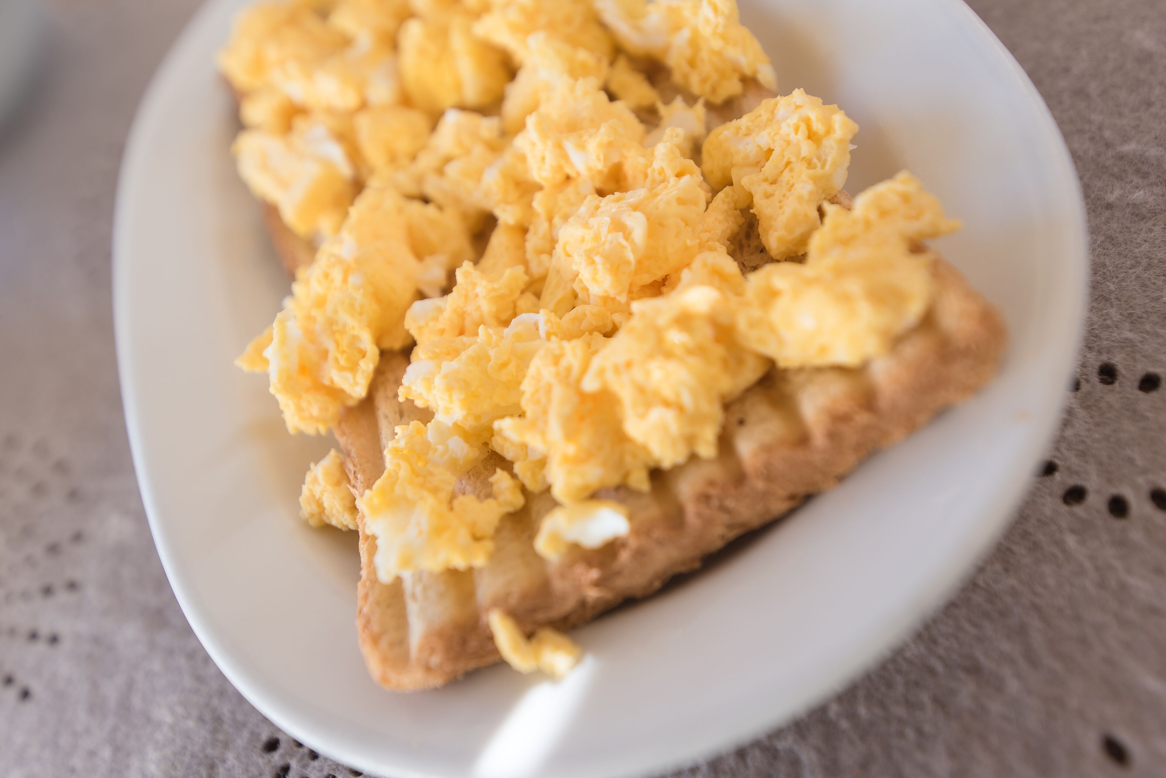 A slice of toast topped with scrambled eggs on a white plate.