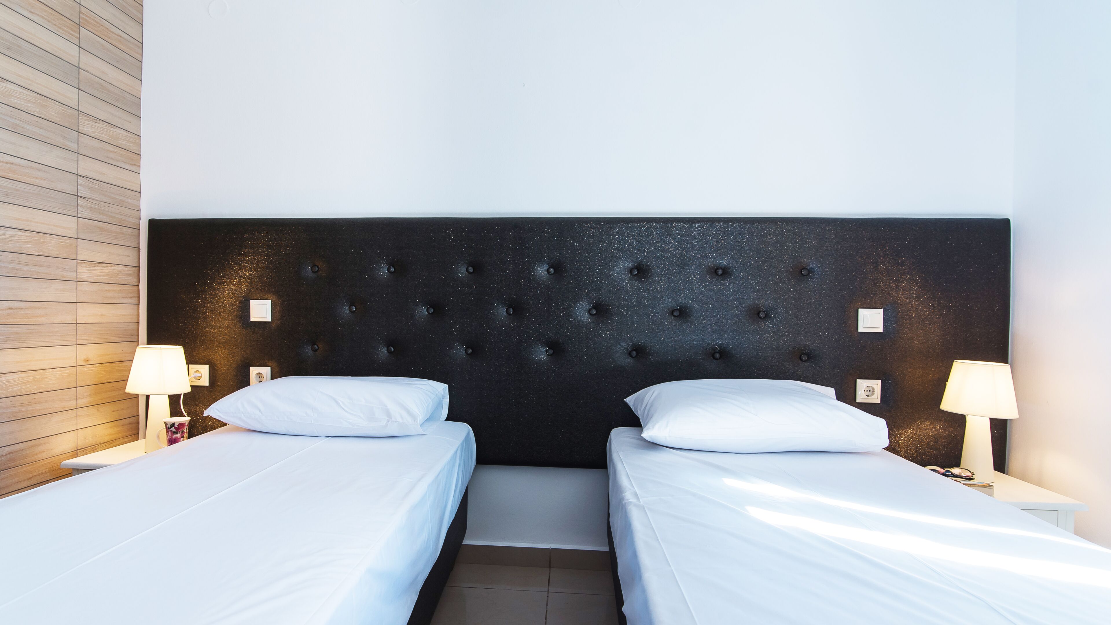 Habitación de hotel con dos camas individuales, cabecera oscura y lámparas de noche.