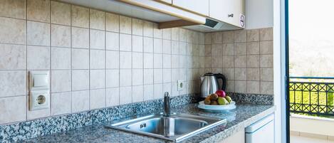 Una cocina con encimera de granito, pileta de acero inoxidable y una cesta de frutas.