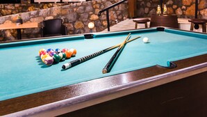 A pool table with billiard balls and cues, surrounded by stone walls and outdoor seating. - Real Palace (Hersonissos)