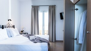 A neatly made bed with white linens, a bedside table with a lamp, and a view of the outdoors through a window with curtains. - Real Palace (Hersonissos)