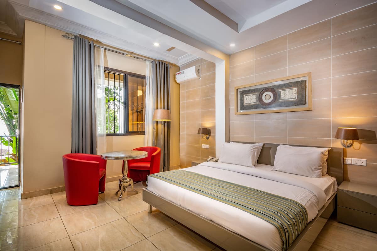 Ein Hotelzimmer mit Bett, einem roten Sessel, einem kleinen Tisch und einem Fenster mit Vorhängen.