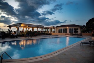 Una piscina con un patio techado, mobiliario exterior y vistas a las montañas.