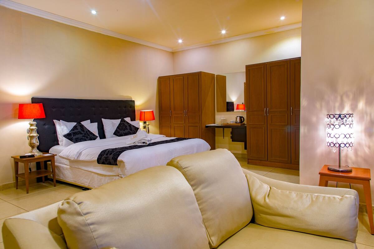 Ein Hotelzimmer mit Bett, Sofa, Nachttisch, Lampe, Kleiderschrank und Spiegel.