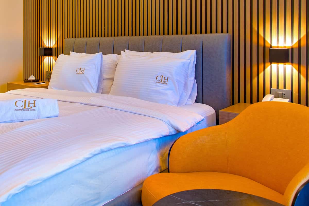 Ein Hotelzimmer mit einem großen Bett, einem Nachttisch, einer Lampe und einem orangefarbenen Sessel.