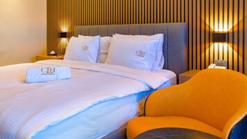 Una habitación de hotel con una cama grande, una mesita de noche, una lámpara y una silla naranja.