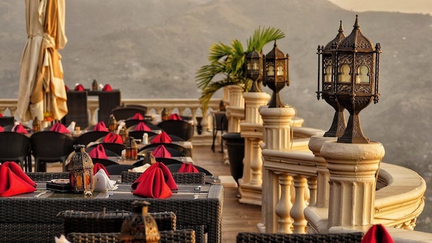 A restaurant with outdoor seating, wicker tables, red napkins, and ornate lanterns. - The Country Lodge Hotel (Freetown)