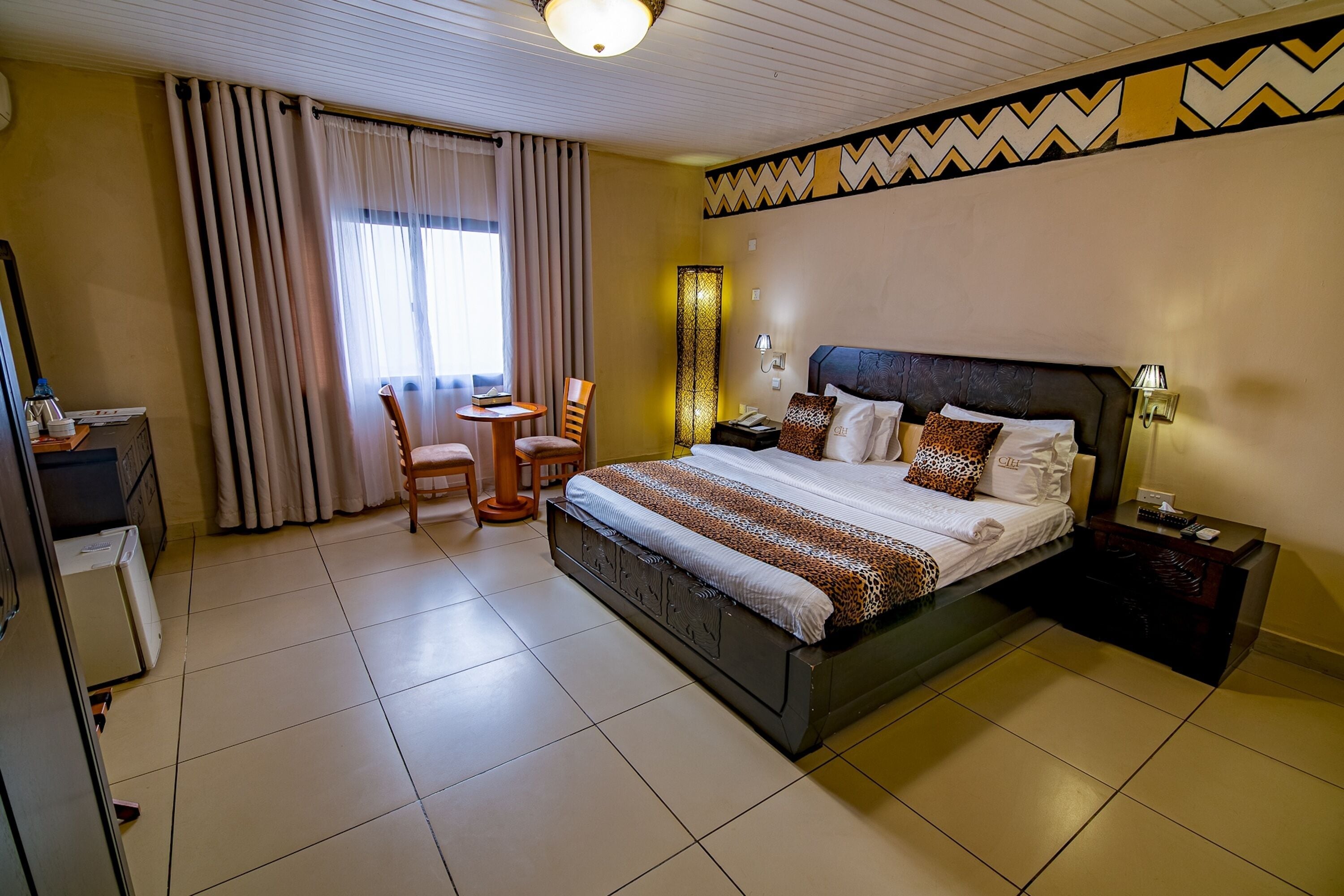 A hotel room with a large bed, a desk, a chair, and a small table.