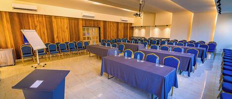 A conference room with rows of blue chairs, tables with water bottles, a podium, and a whiteboard.