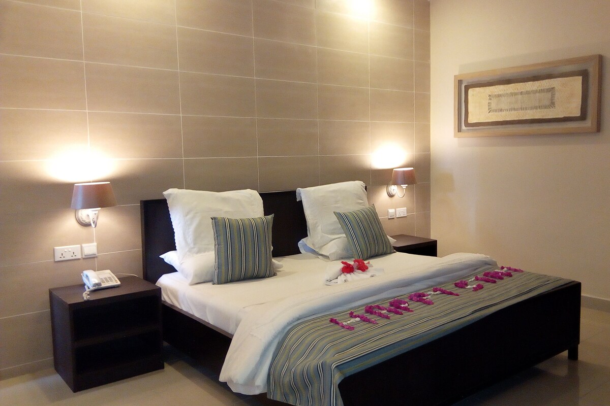 A neatly made bed with pillows, a bedside lamp, a phone, and a framed picture on the wall.