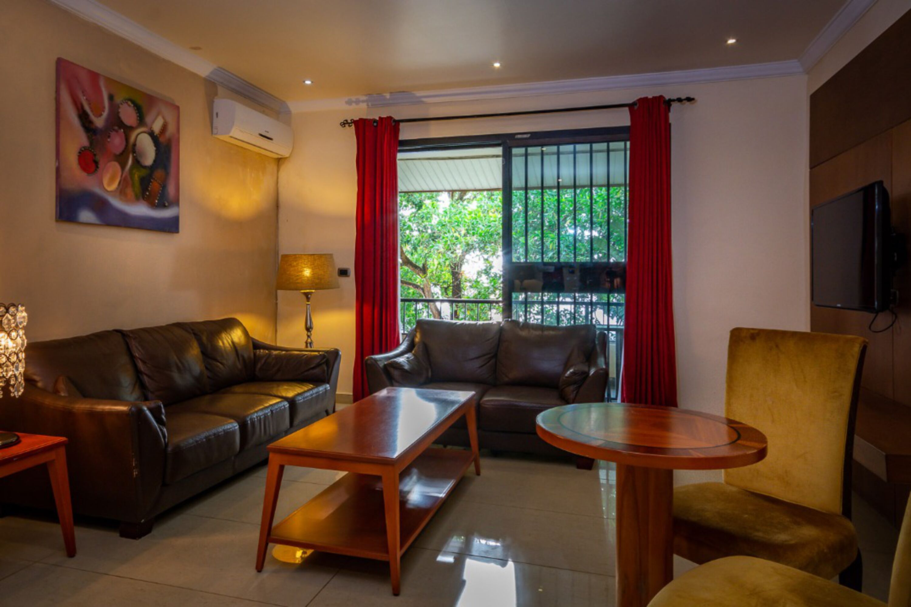 A living room with a brown leather sofa, a wooden coffee table, a yellow armchair, and a TV on the wall.