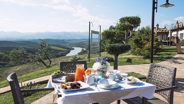 An outdoor dining table with breakfast items, overlooking a scenic valley and river. - Agriturismo Podere Diacceroni (Peccioli)