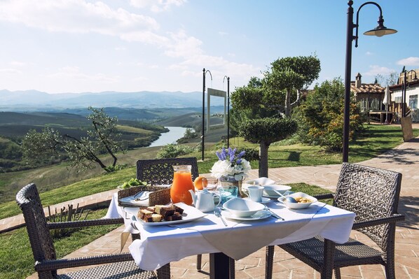 Une table à manger en plein air, dressée pour le petit-déjeuner, avec vue sur une vallée et une rivière pittoresques.