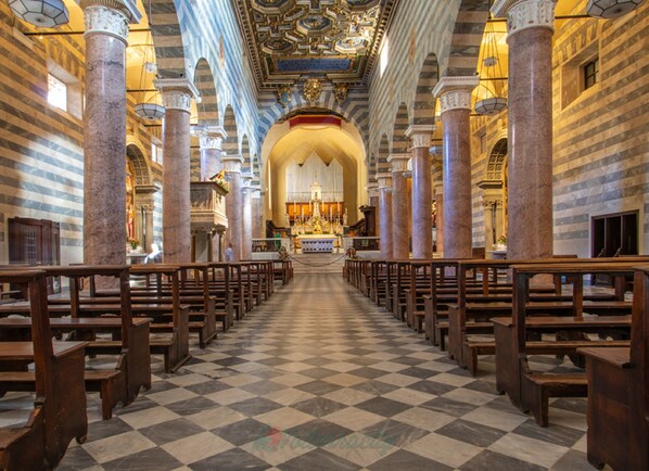 L’intérieur d’une église avec un sol à carreaux, des bancs en bois et des colonnes en marbre.