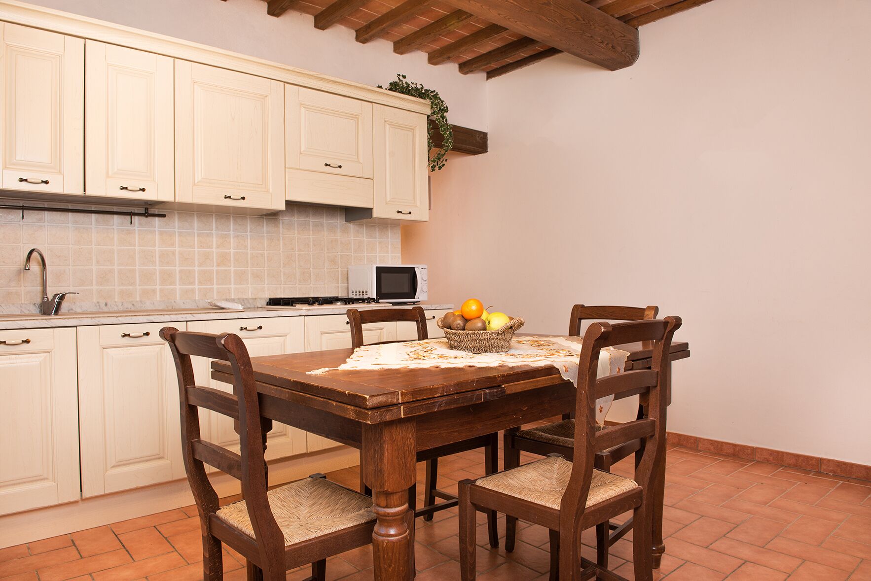 Una cocina con armarios blancos, salpicadero de azulejos, microondas y una mesa de comedor con sillas.