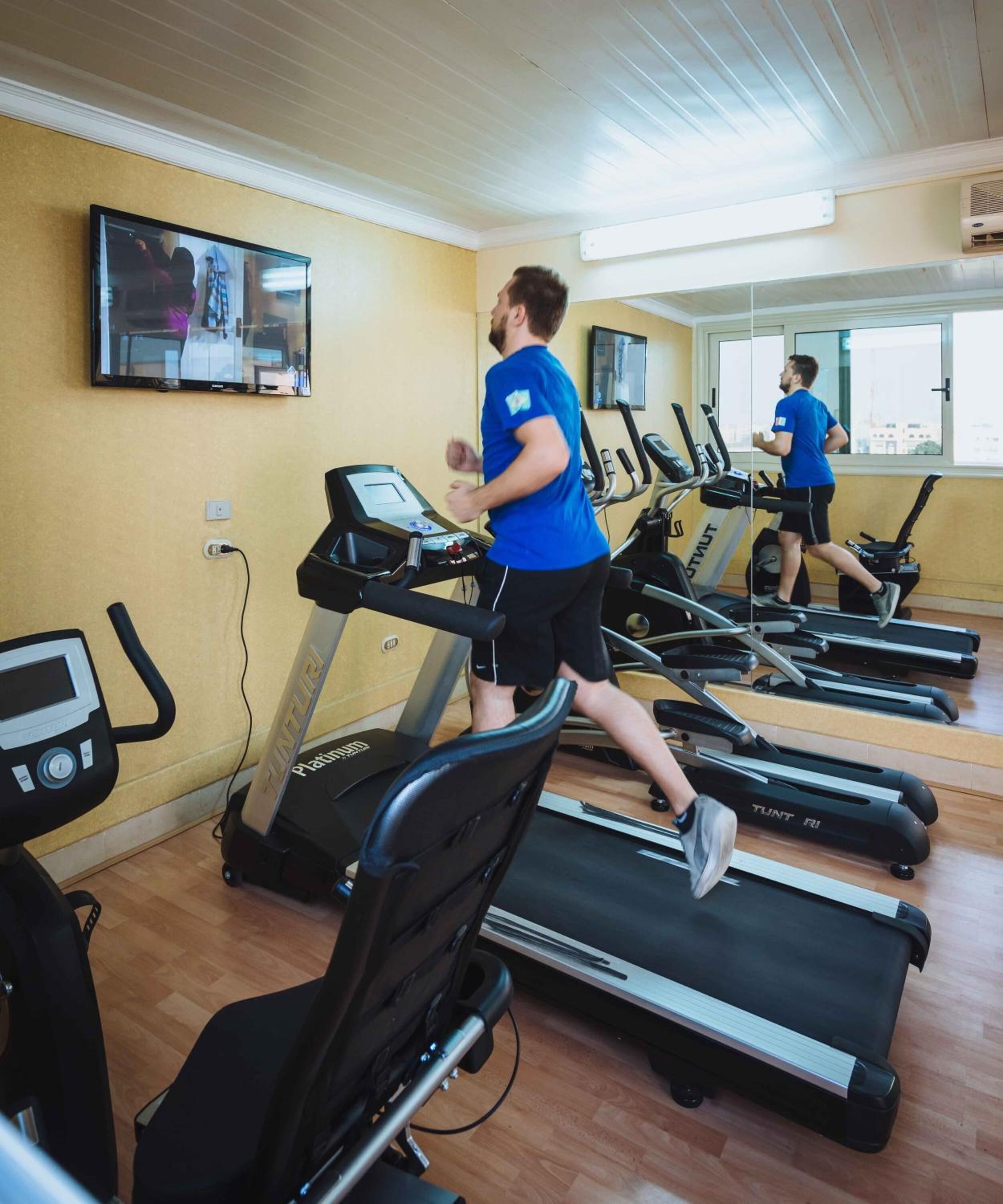 Un gimnasio con varias cintas de correr, un televisor montado en la pared y un ventanal que proporciona luz natural.
