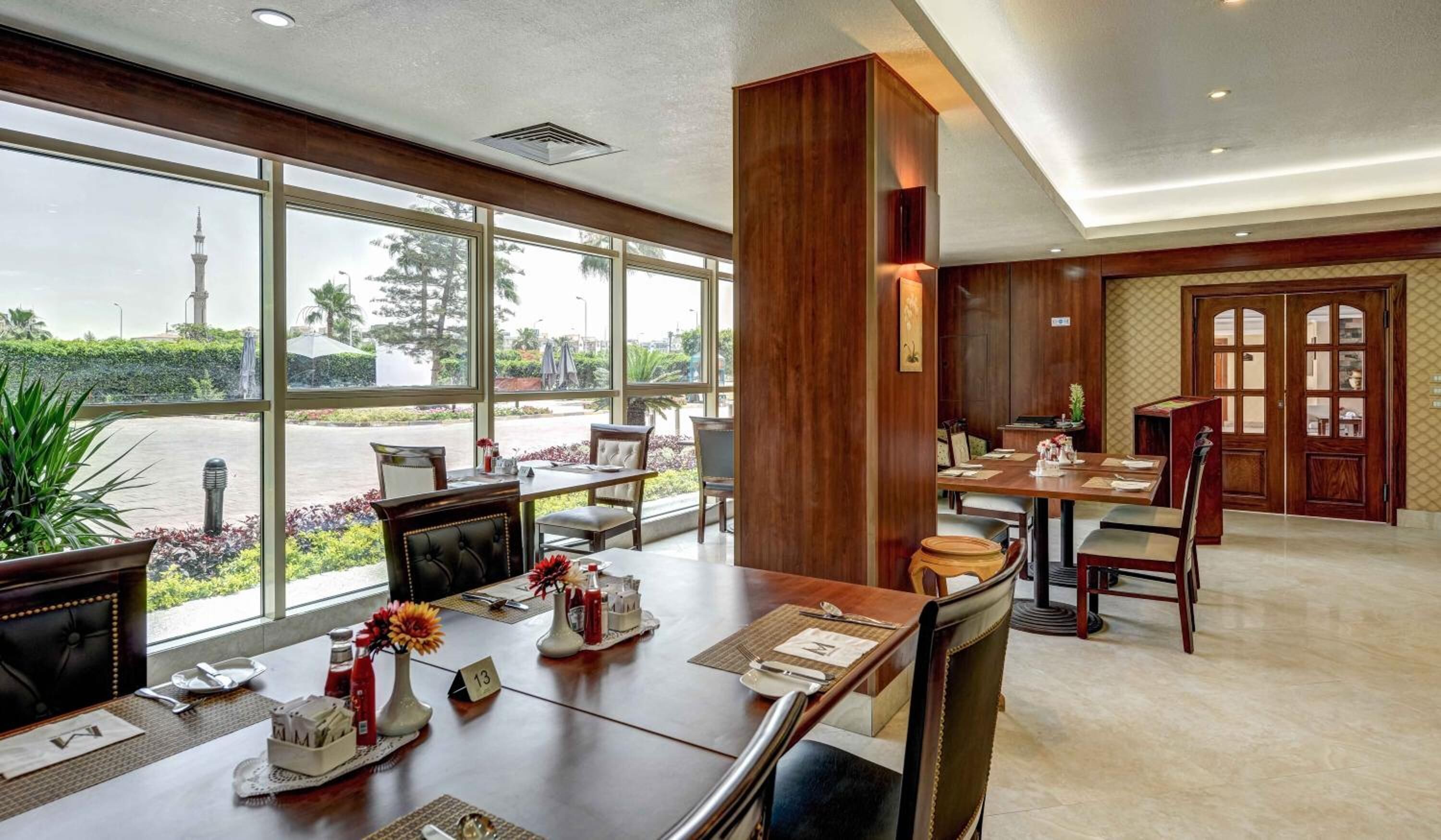 Comedor de hotel con ventanas amplias, mobiliario de madera y vista a una torre.