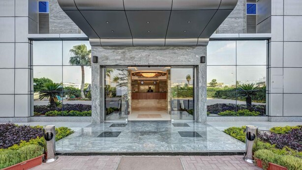 A modern hotel entrance with a reception desk, glass doors, and a landscaped garden. - Mirita Hotel (Tenth of Ramadan City)