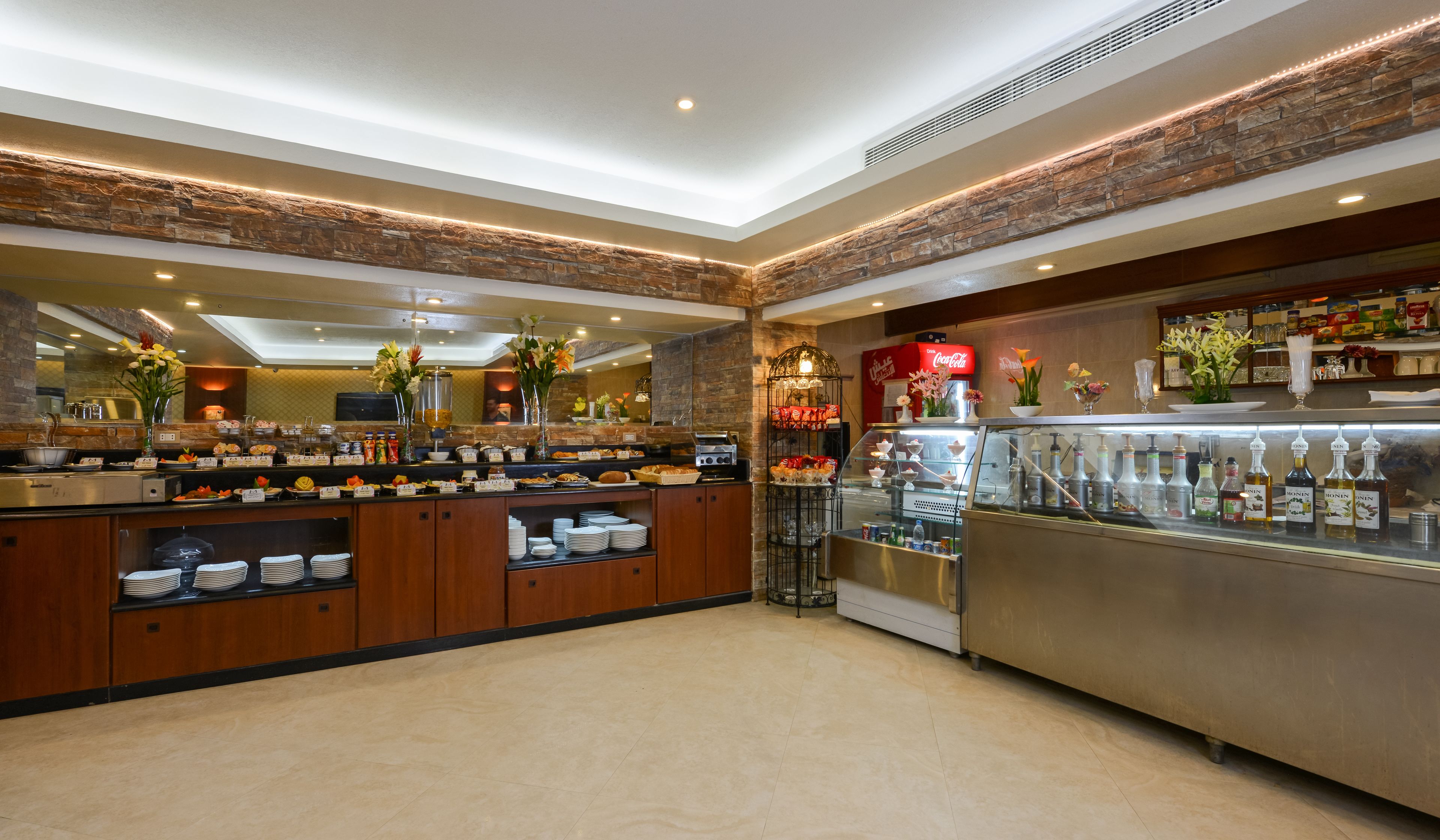 Uma área de buffet com diversos pratos, um refrigerador de Coca-Cola e uma seleção de bebidas.