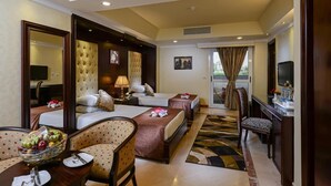 A hotel room with two beds, a sitting area with a table and chairs, a TV, and a large window with curtains. - Mirita Hotel (Tenth of Ramadan City)