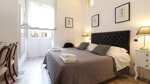 A neatly made bed with a dark headboard, a bedside table with a lamp, and a chair to the left.