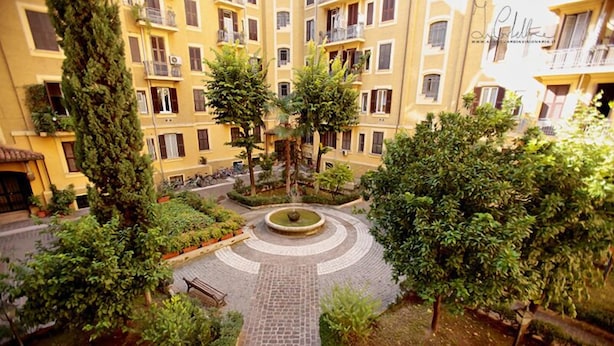 A courtyard with a central fountain, surrounded by trees and a paved walkway.