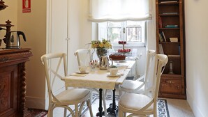 A dining area with a chandelier, white chairs, a table with a vase of flowers, and a bookshelf.